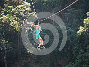 Brave little boy in helmet and harness zip lining at adventure park