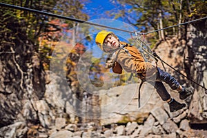 Brave little boy rappelling high among the trees in an Adventure Park for children. Extreme kid. The boy goes down the