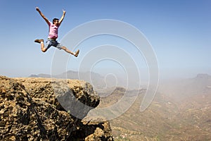 Brave man on pink t shirt jumping high up on rock edge