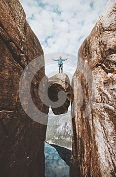 Brave man traveler standing on Kjeragbolten raised hands