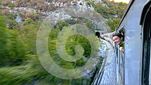 A brave young girl leans out the window fast moving train approaching the tunnel. She laughs and happy journey