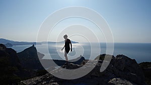 Brave young girl walks on top of a cliff and enjoys the beautiful view of the sea and the brightest sun above it, front