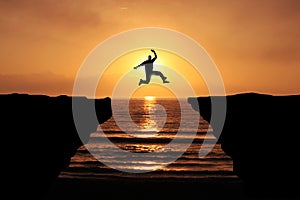Brave Young Man jumping over the cliff, silhouette Sunset background. Business Goal Achieve concept