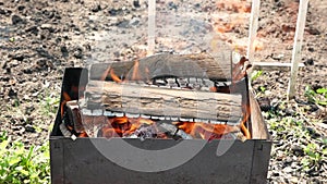 Brazier close-up in which firewood is burning with a bright flame. Burning logs for charcoal barbecue during the daytime. Fire fro