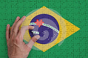 Brazil flag is depicted on a puzzle, which the man`s hand completes to fold