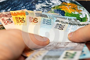 brazil money, hands holding brazilian reais over world map, financial business concept, world currency, global economy