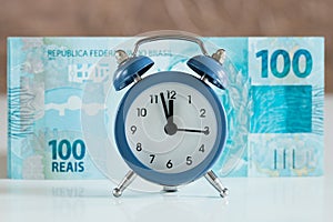 Brazilian banknote, one hundred Reals, In front of him an alarm clock set to five to twelve, Concept