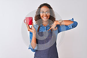 Brazilian barista woman wearing apron drinking cup of coffee over isolated white background with surprise face pointing finger to