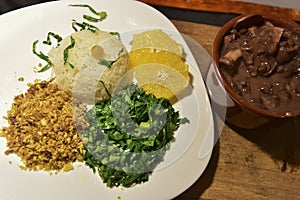 Brazilian beans and pork feijoada, with rice flour salad over piece of wood with blurs