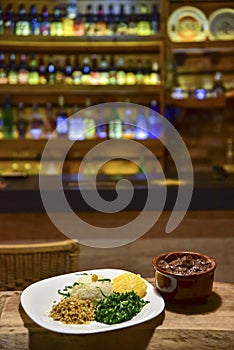 Brazilian beans and pork feijoada, with rice flour salad over piece of wood with blurs