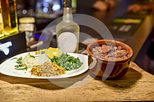 Brazilian beans and pork feijoada, with rice flour salad over piece of wood with blurs
