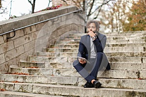 Mulatto businessman using tablet and sitting on steps.