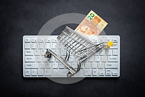 Brazilian cash, White computer keyboard, Miniature shopping cart, Black background, Online shopping concept in stores, Low prices