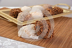 Brazilian cocada coconut candy placed on a golden tray and wooden mat on a table with white towel, selective focus