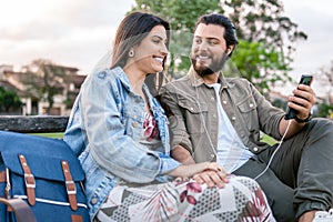 Couple listening music on mobile phone with headphones in bench park