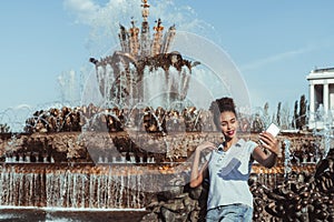 Brazilian girl is taking selfie next to fountain using cellphone