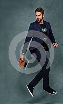 Brazilian man, suit and jumping in studio with notebooks, fashion and joy on grey background. Male model, dance and