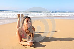 Brazilian smiling beautiful girl lying down on sand enjoying sun tanning sunbathing in swimsuit relaxing on Canary Island tropical