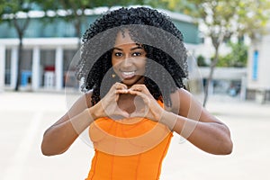 Brazilian woman with orange dress showing heart with fingers