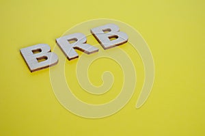 BRB wooden letters representing Be Right Back on yellow background