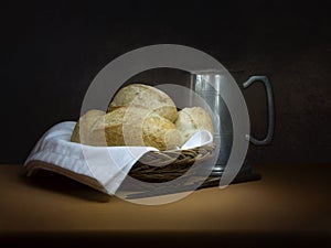 Bread and ale, rustic lunch, with old pewter tankard, bread rolls and knife. Painting like chiaroscuro still life. photo