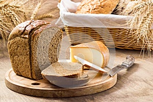 Bread and cheese sliced for sandwiches amid the loaves in a wicker basket with ears of wheat