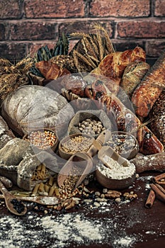 Bread background. Brown and white whole grain loaves wrapped in kraft paper composition on rustic dark wood with wheat ears scatte