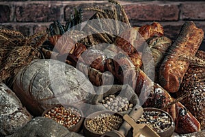 Bread background. Brown and white whole grain loaves wrapped in kraft paper composition on rustic dark wood with wheat ears scatte