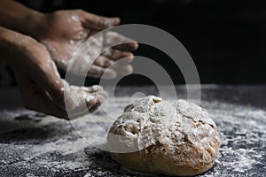 Bread baking concept.Hands with flour and traditional bread on floury table with black background.Copy space