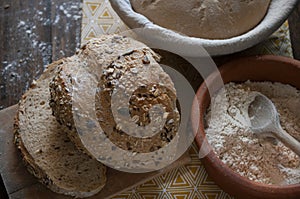 Bread baking, flour in ceramic bawl with wooden spoon, bread with seeds, sourdough dough in basket