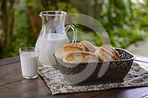 Bread in a basket and milk in a glass jug on a wooden table