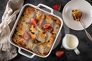 Bread and butter pudding with raisins and fresh strawberry in white baking dish