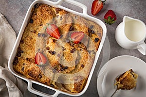 Bread and butter pudding with raisins and fresh strawberry in white baking dish