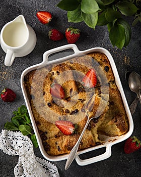 Bread and butter pudding with raisins and fresh strawberry in white baking dish