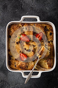 Bread and butter pudding with raisins and fresh strawberry in white baking dish