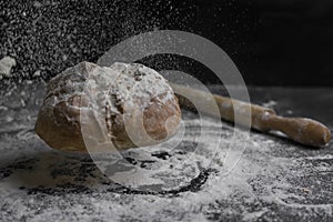 Bread flying with flour splash and rolling pin on floury black table.Concept of bakery, baking and cooking .Copy Space