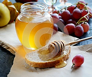 Bread with honey on paper, ripe grapes, nuts and apples on a dark background