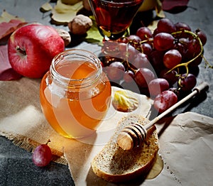 Bread with honey on paper, ripe grapes, nuts and apples on a dark background