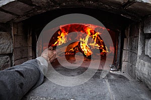 Bread oven with a fire inside, while man is adding some wood to the fire