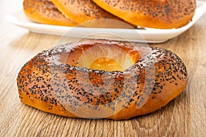 Bread rings with poppy in white plate on background, single baranka on table