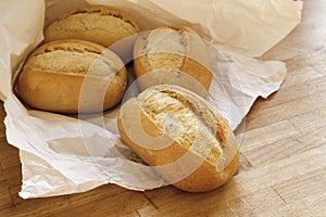 bread rolls or buns for breakfast fresh from the bakery in a white paper bag on a wooden table