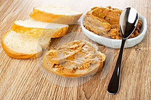 Bread, sandwich with peanut pasta, spoon on blue bowl with peanut butter on table