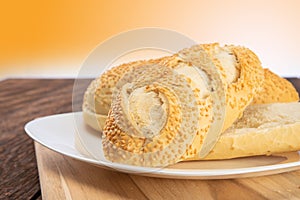 Bread with sesame cut in half on a white plate on a wooden table with an orange background, selective focus