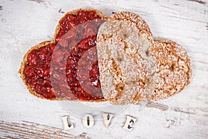 Bread in shape of heart with strawberry jam and inscription love. Rustic background