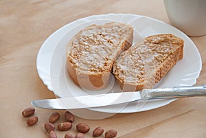 Bread slice with peanut butter, peanuts, a cup of coffee and knife on a wooden table. Top view