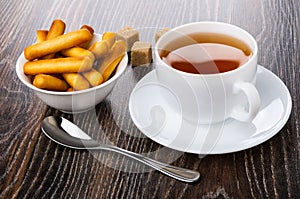 Bread sticks in bowl, sugar, teaspoon, tea in cup on saucer on t