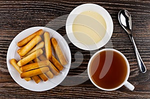 Bread sticks in saucer, bowl with condensed milk, teaspoon, tea