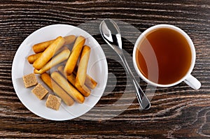 Bread sticks in saucer, teaspoon, tea on table. Top view