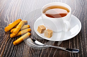 Bread sticks, teaspoon, tea in cup, sugar on saucer on table