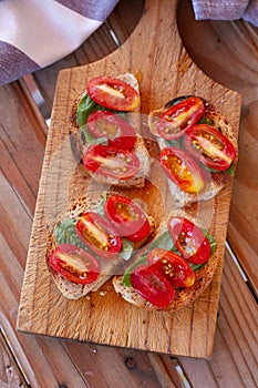 Bread toasts with cherry tomato and basil leaves on a wooden kitchen board